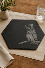 Hexagonal black slate placemat featuring a detailed illustration of an owl wearing round glasses and a top hat, displayed on a beige linen runner over a wooden table with a glass of water and a small plant.