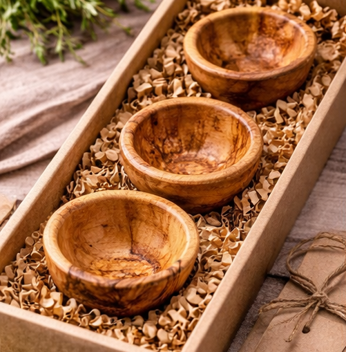Three wooden bowls in a box with shredded paper on a rustic background