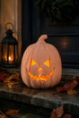 A carved jack-o'-lantern pumpkin with a glowing orange light inside, placed on a stone step beside a black lantern and autumn leaves.