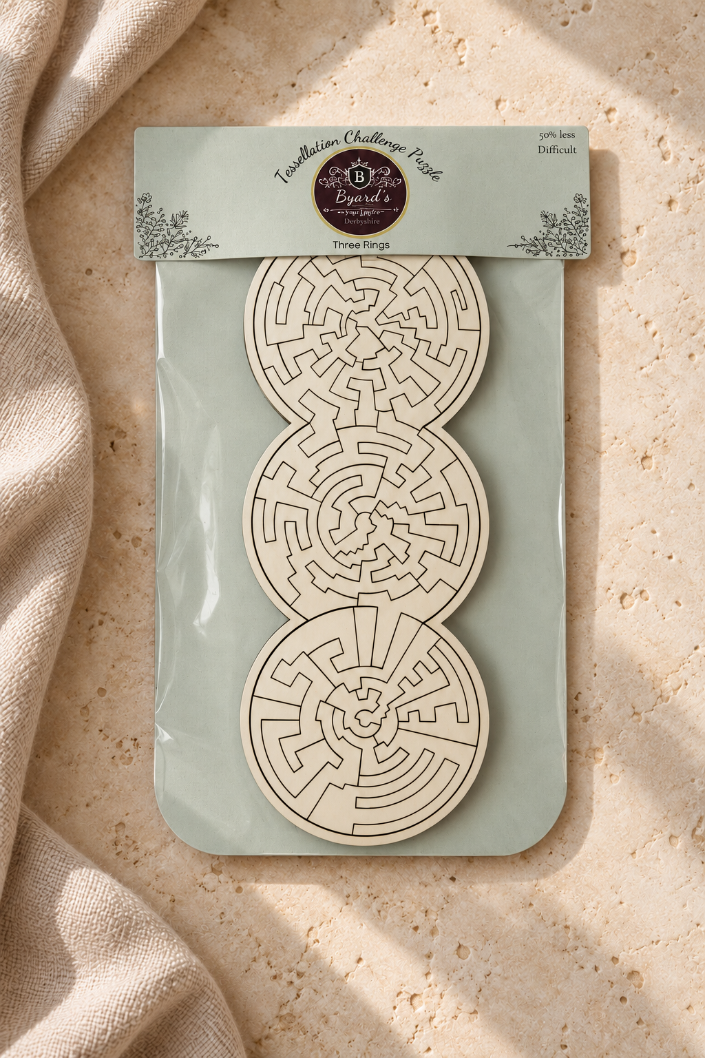 Three Rings easier wooden puzzle in its packaging on pale limestone and linen, showing white pieces and intricate laser-cut shapes.