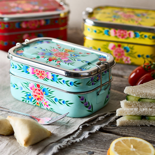 Floral-patterned metal lunch box on a wooden table with sandwiches and lemon