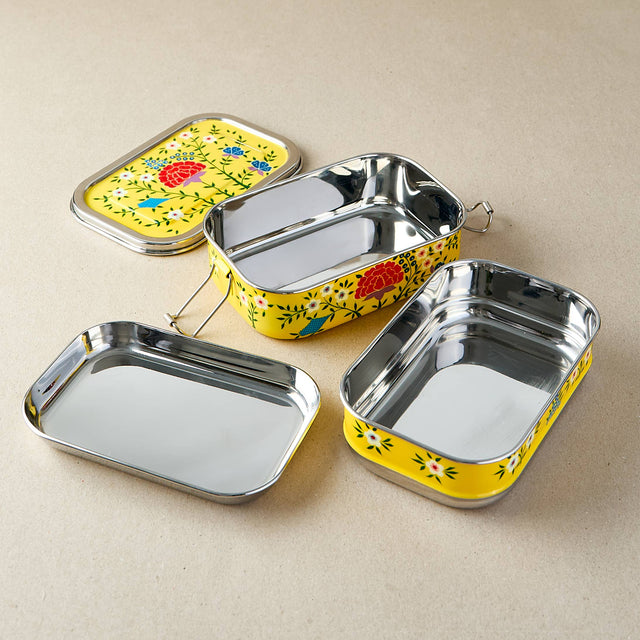 Set of three metal lunch boxes with floral designs on a beige background