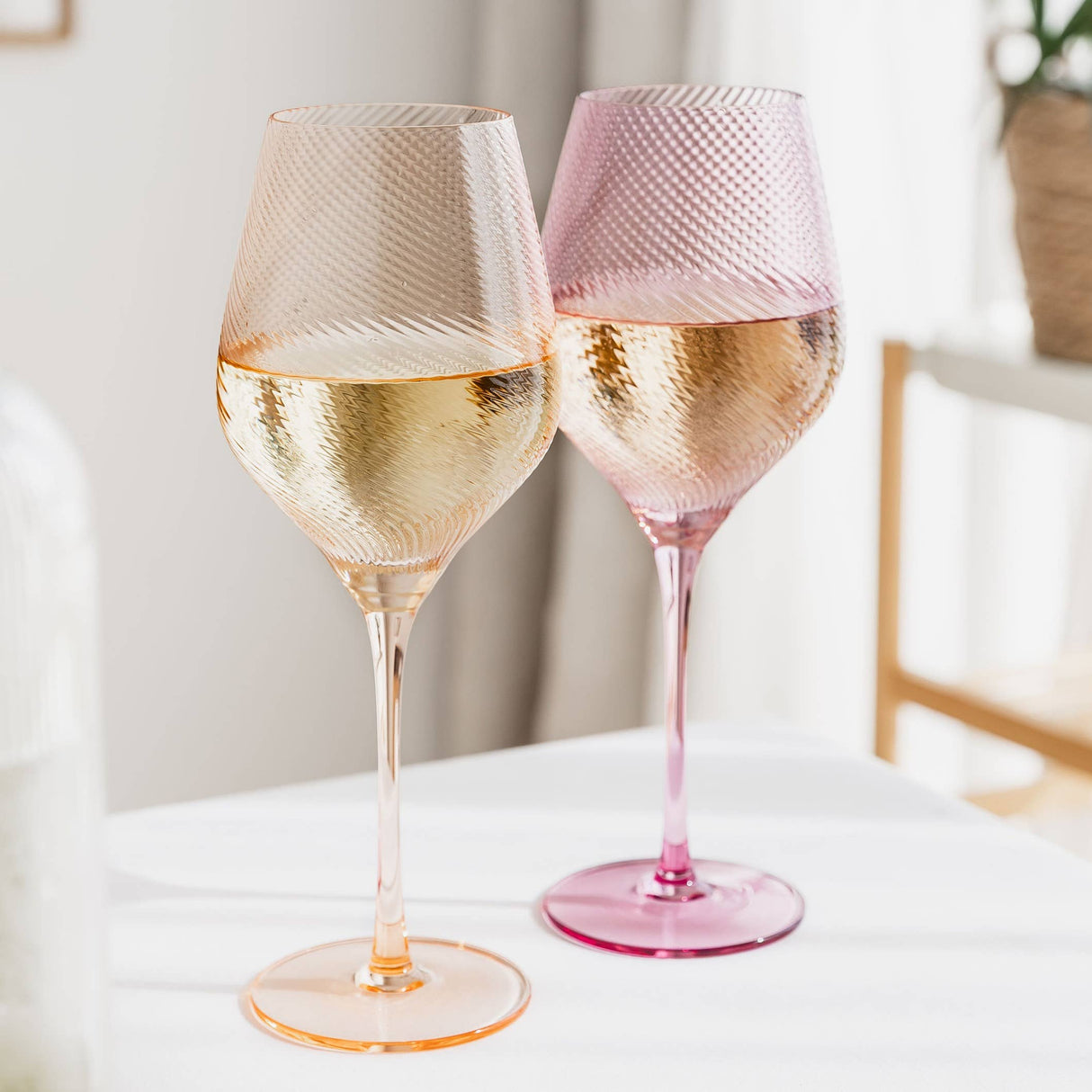 Two twisted wine glasses filled with white wine on a light surface.