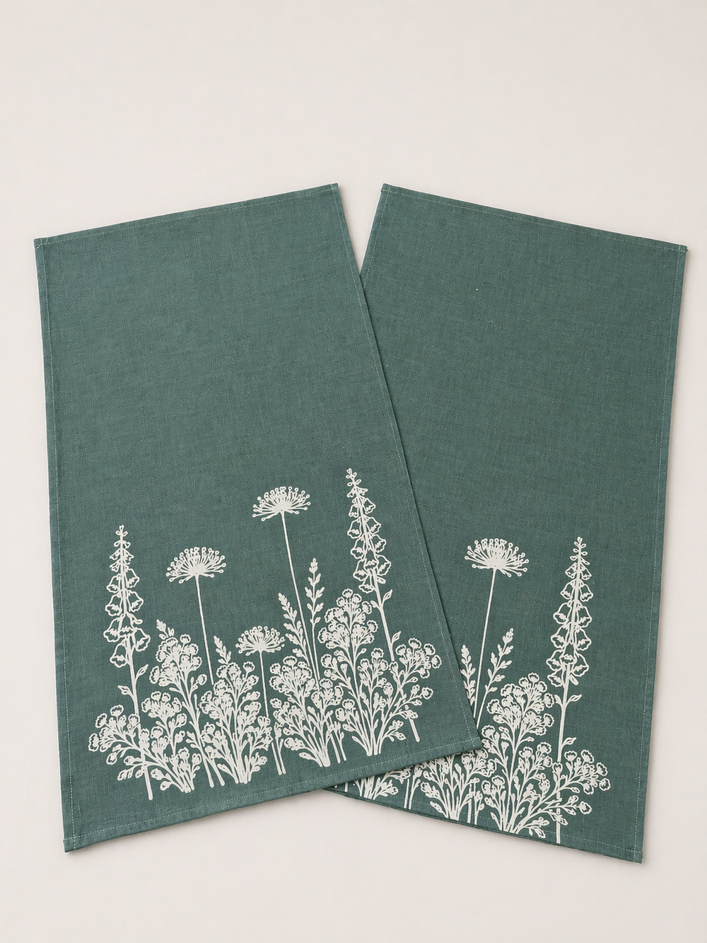 Two linen tea towels with white floral patterns on a light background