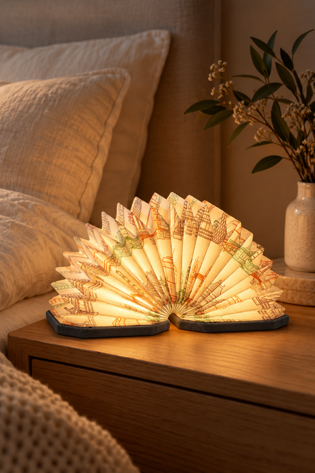 Grey Landmark Velvet Accordion Lamp glowing warmly on an oak bedside table beside cream linen bedding.
