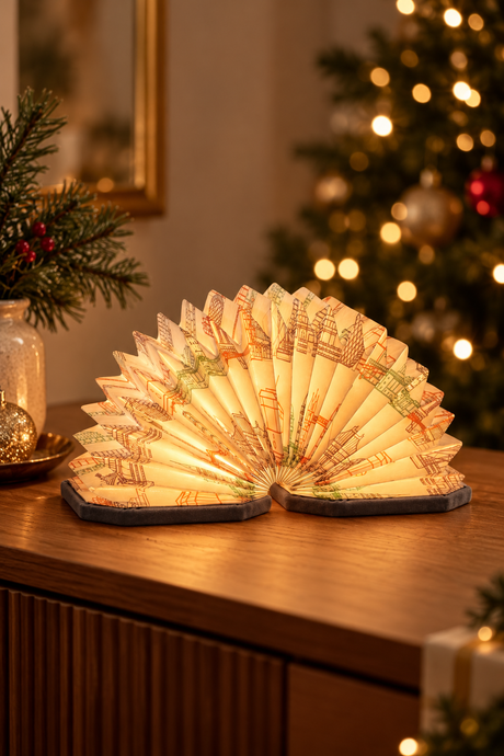 Grey Landmark Velvet Accordion Lamp glowing on a wooden console with soft Christmas tree lights in the background.