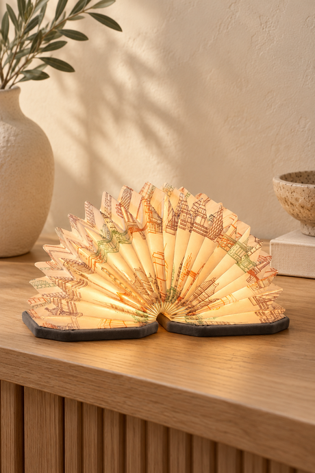 Grey Velvet Landmark Print Accordion Lamp opened into a glowing fan on an oak console, showing architectural illustrations and grey velvet covers.