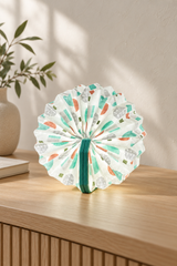 Turquoise Velvet Geometric Print Accordion Lamp opened into a circle on an oak console, showing colourful geometric pleats and turquoise velvet covers.