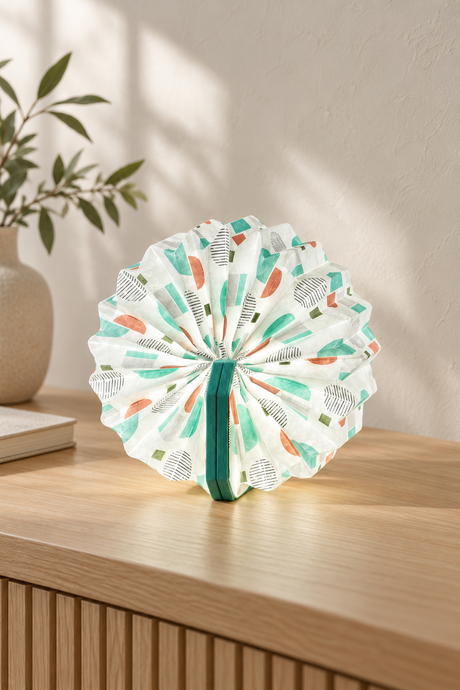 Turquoise Velvet Geometric Print Accordion Lamp opened into a circle on an oak console, showing colourful geometric pleats and turquoise velvet covers.