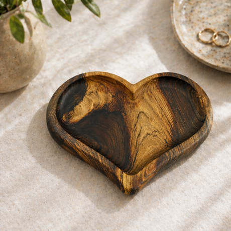 Heart-shaped wooden tray made from walnut on a marble surface with a glass of water and a plant.