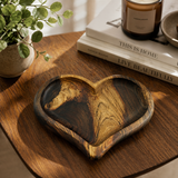 Wooden heart-shaped tray on a wooden surface with books and a plant in the background