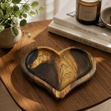 Wooden heart-shaped tray on a wooden surface with books and a plant in the background