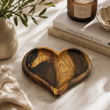 Wooden heart-shaped dish on a marble surface with books and a candle in the background
