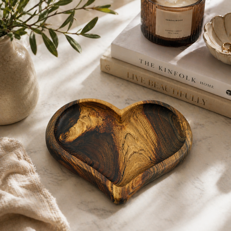 Wooden heart-shaped dish on a marble surface with books and a candle in the background