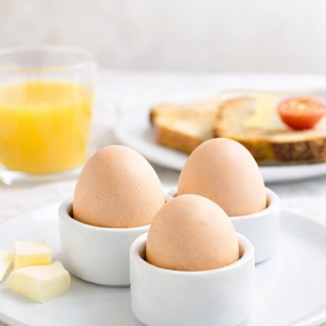 eggs in white cups with breakfast items like toast, orange juice,