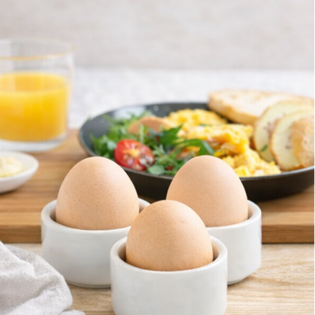 eggs in white cups with breakfast items like toast, orange juice, 