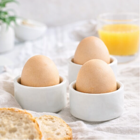eggs in white cups with breakfast items like toast, orange juice.