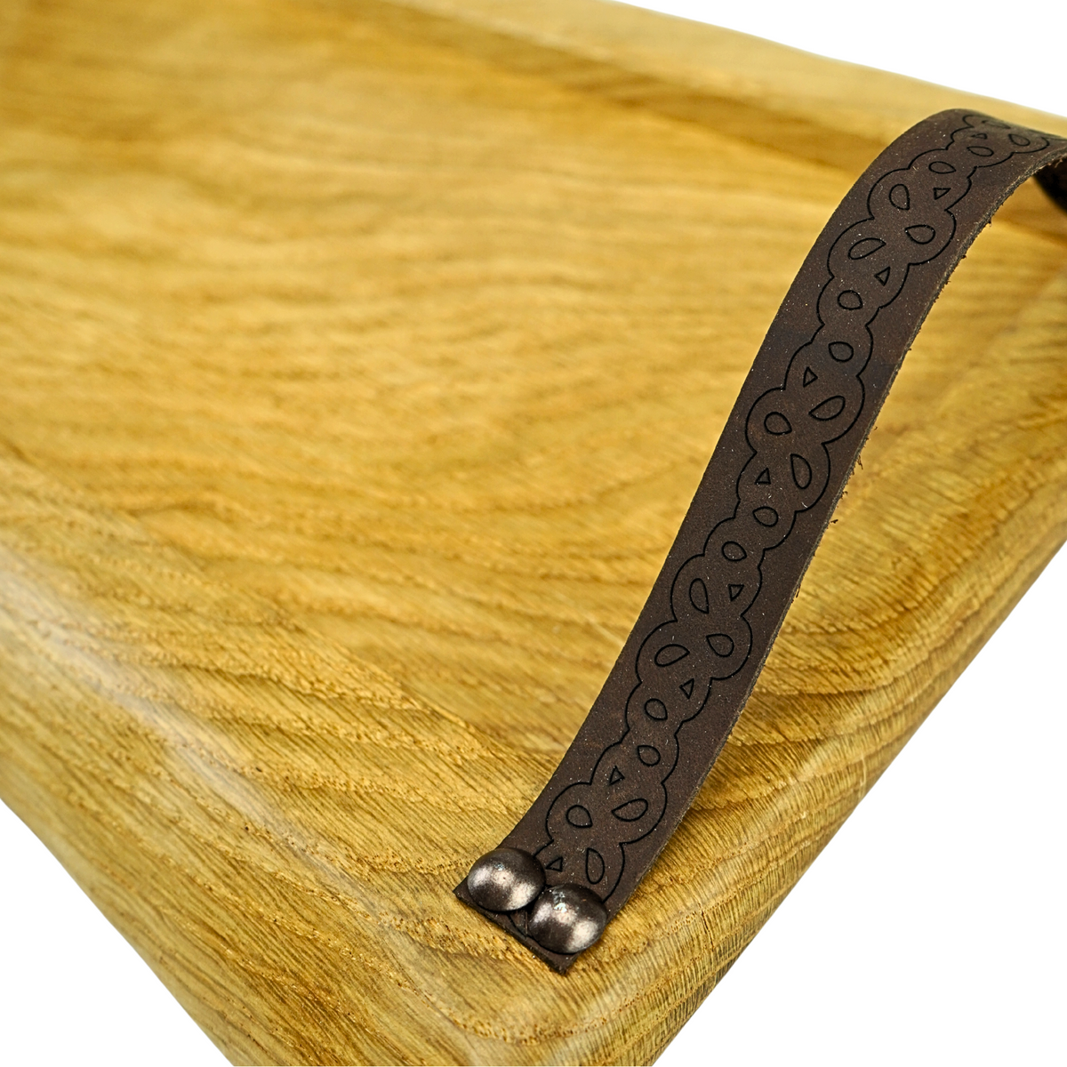 Solid oak serving tray with gently waney edges on both sides and leather handles engraved with a floral pattern. Handles are secured with metal studs.