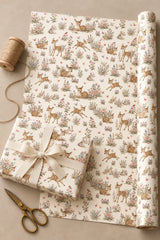 Woodland fawn paper unrolled beside a cream-ribbon gift, showing deer, rabbits and wildflowers.