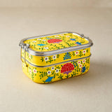 Stackable yellow tiffin tin containers with floral patterns on a beige background