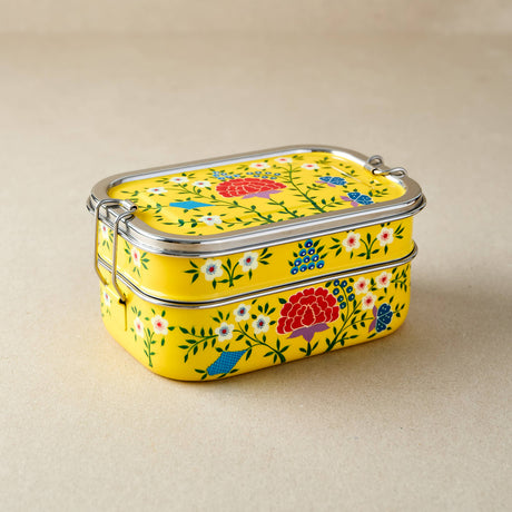 Stackable yellow tiffin tin containers with floral patterns on a beige background