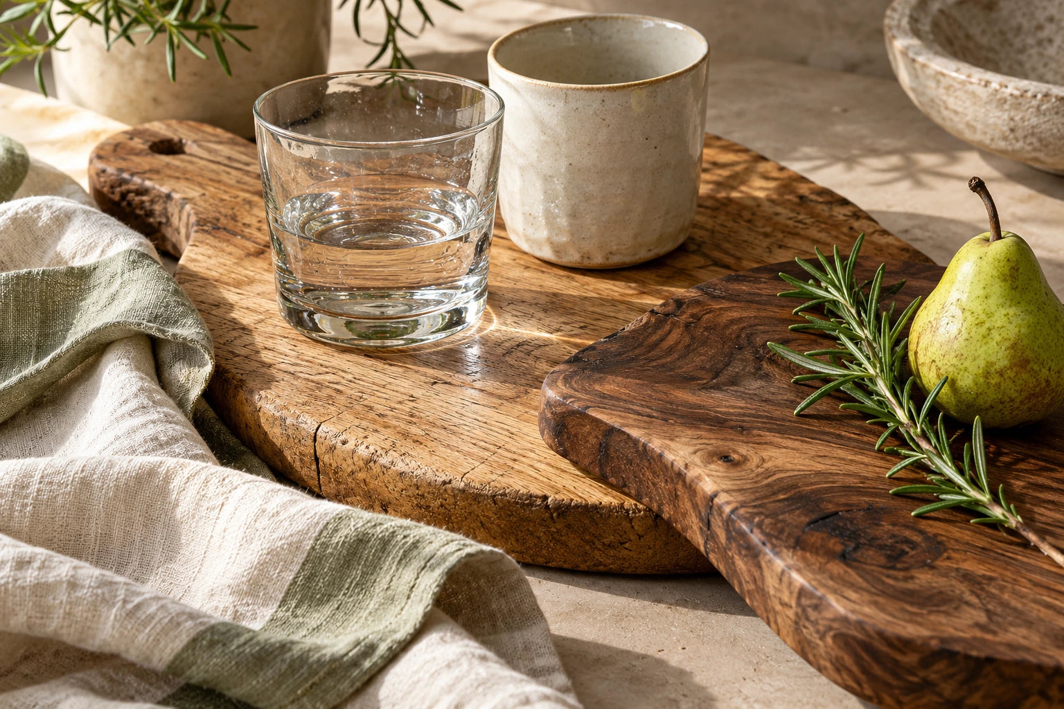 Wooden boards with a linen cloth, clear glass, a ceramic cup, rosemary and a pear.