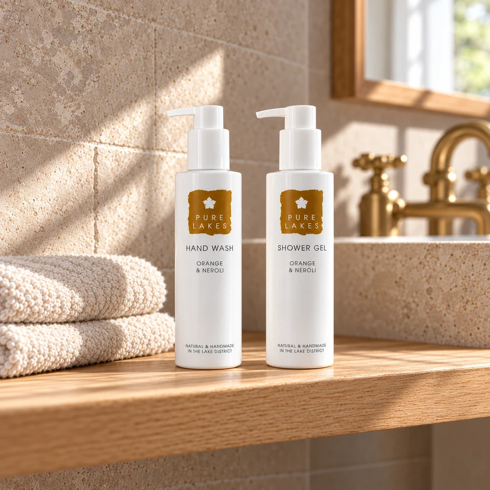 Pure Lakes Orange & Neroli hand wash and shower gel beside cream towels in a softly lit cottage bathroom.